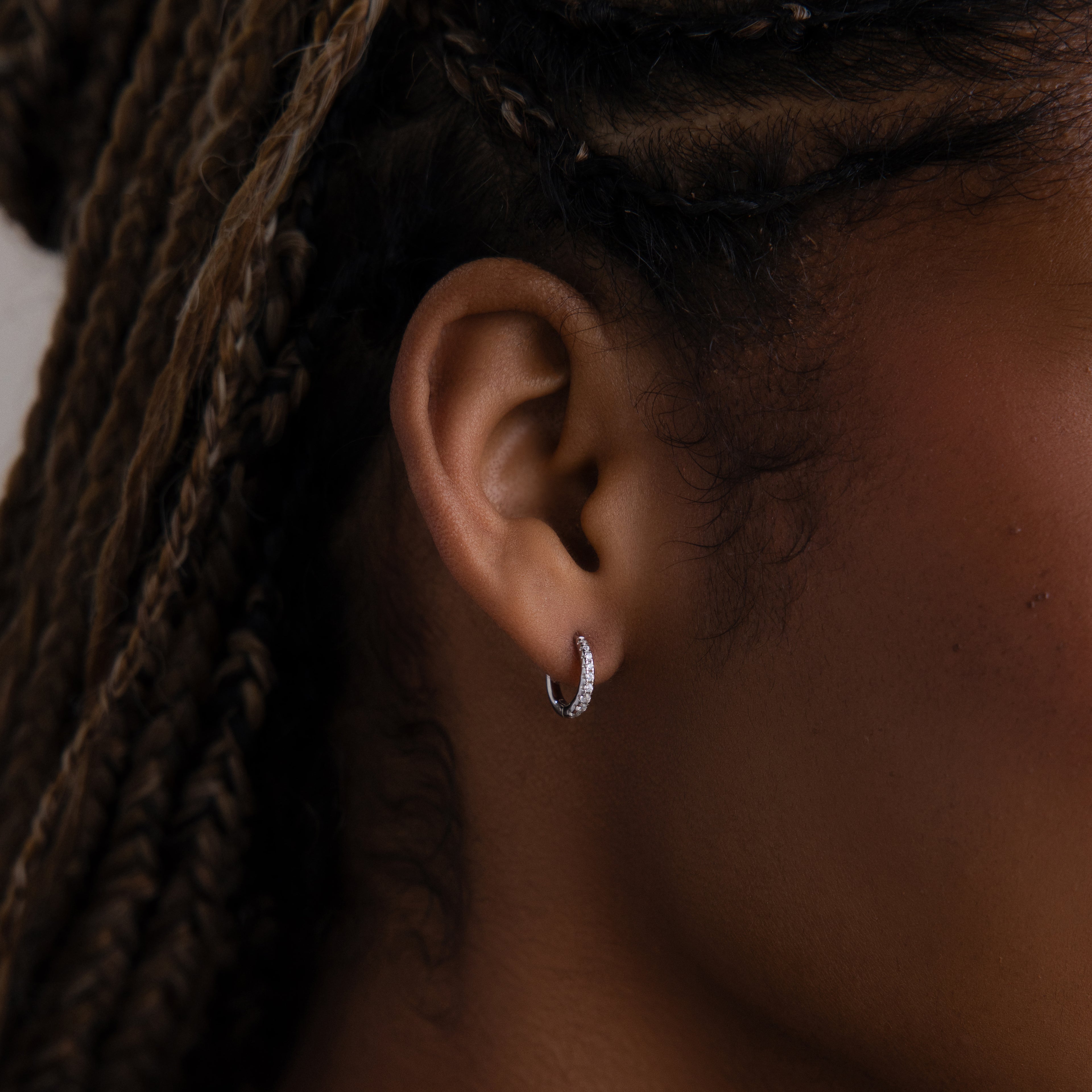 Close-up of an model with a silver diamond hoop earring, hair styled in braids