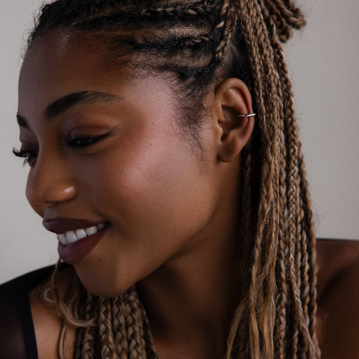 Woman with braided hair and a silver cuff earring smiling against a neutral background