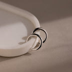 Silver cuff earrings on a beige surface with a soft focus background