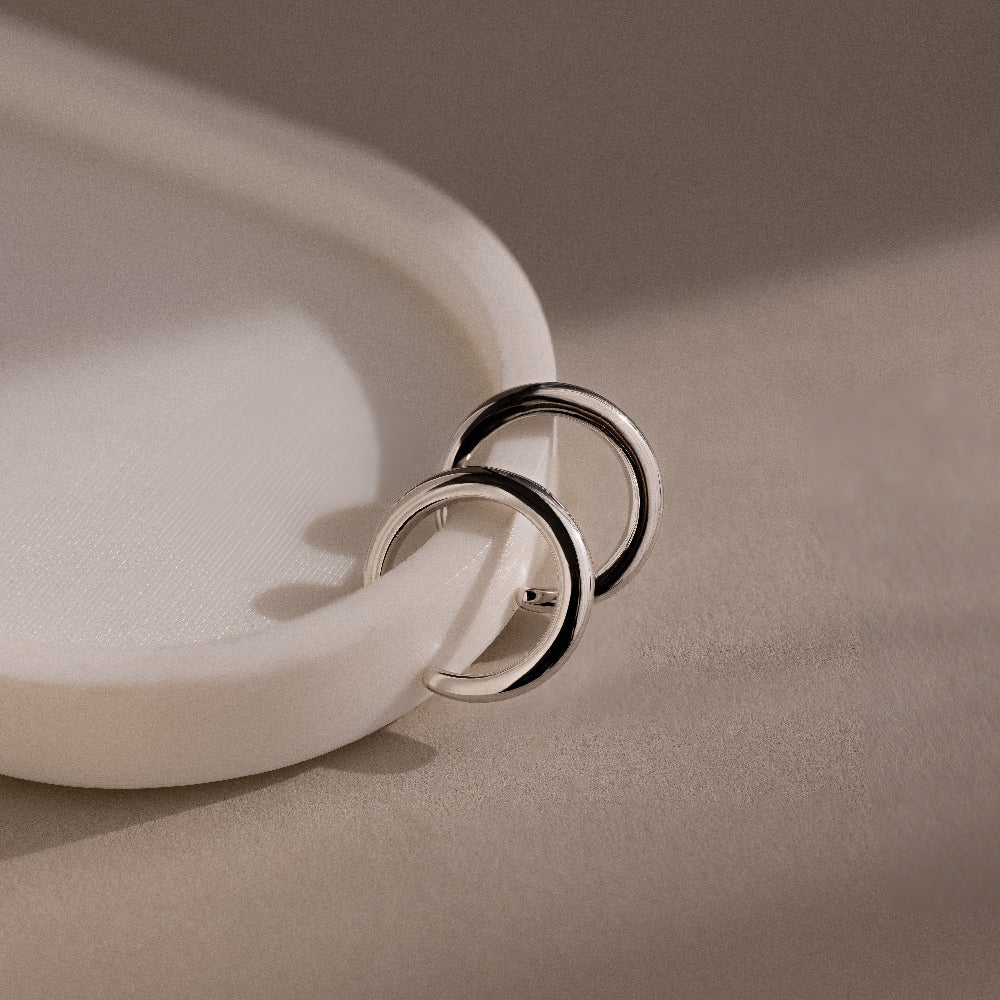 Silver cuff earrings on a beige surface with a soft focus background