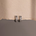 Pair of silver chain hoop earrings on a textured beige surface.