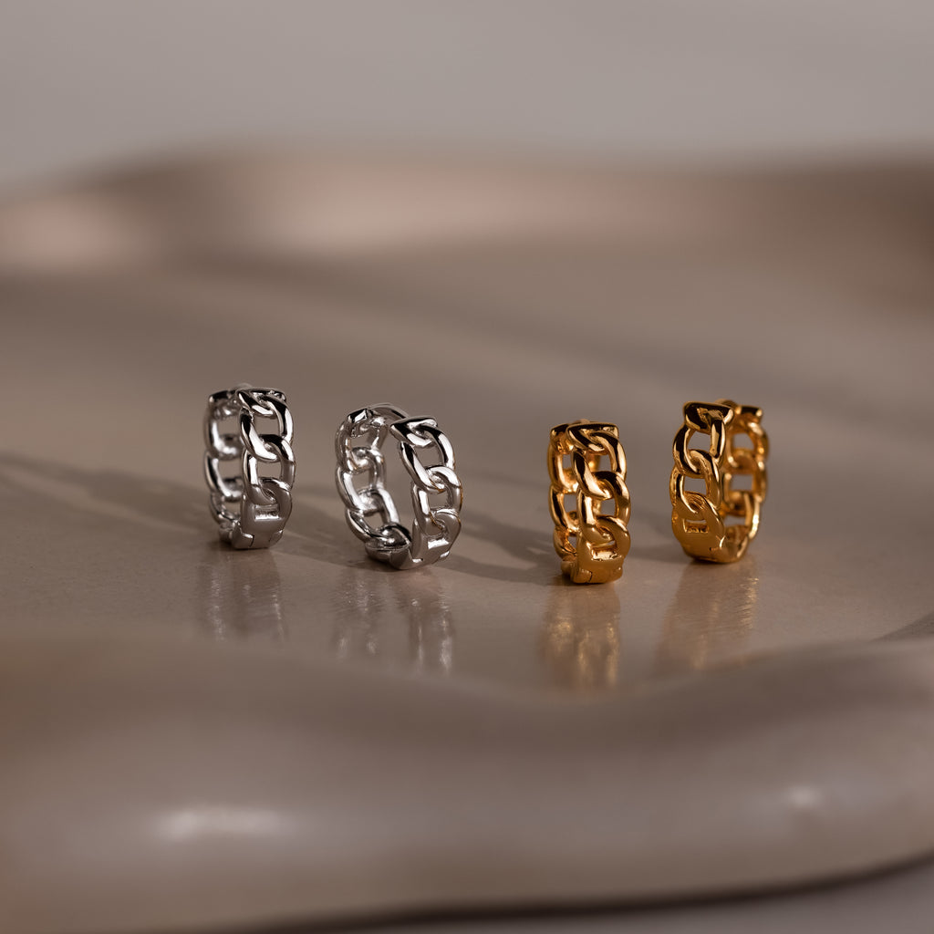 Four chain-link earrings in silver and gold on a reflective surface.