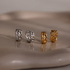 Four chain-link earrings in silver and gold on a reflective surface.
