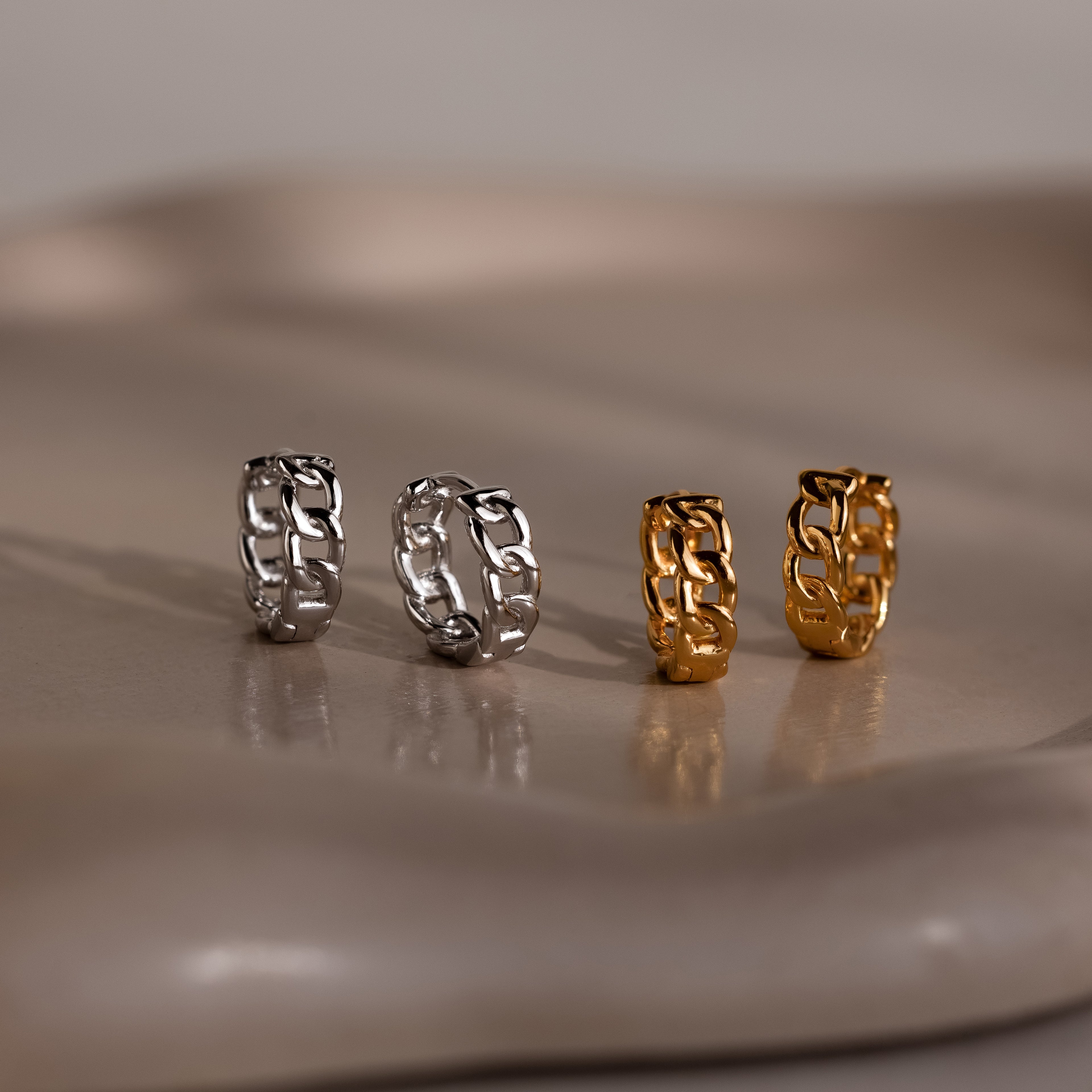 Four chain-link earrings in silver and gold on a reflective surface.