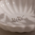 Silver butterfly-shaped diamond earrings on a soft fabric background