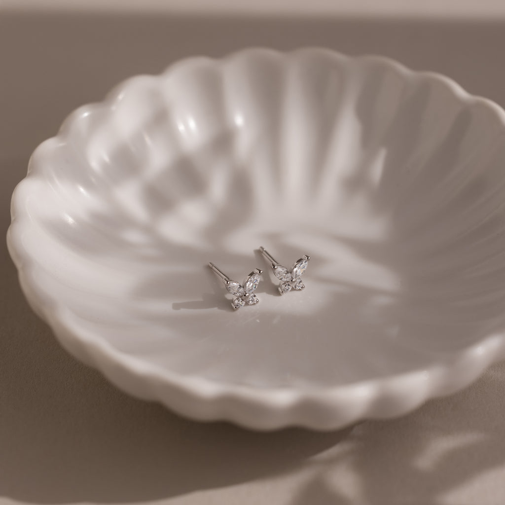 Pair of silver butterfly-shaped earrings on a textured white dish.