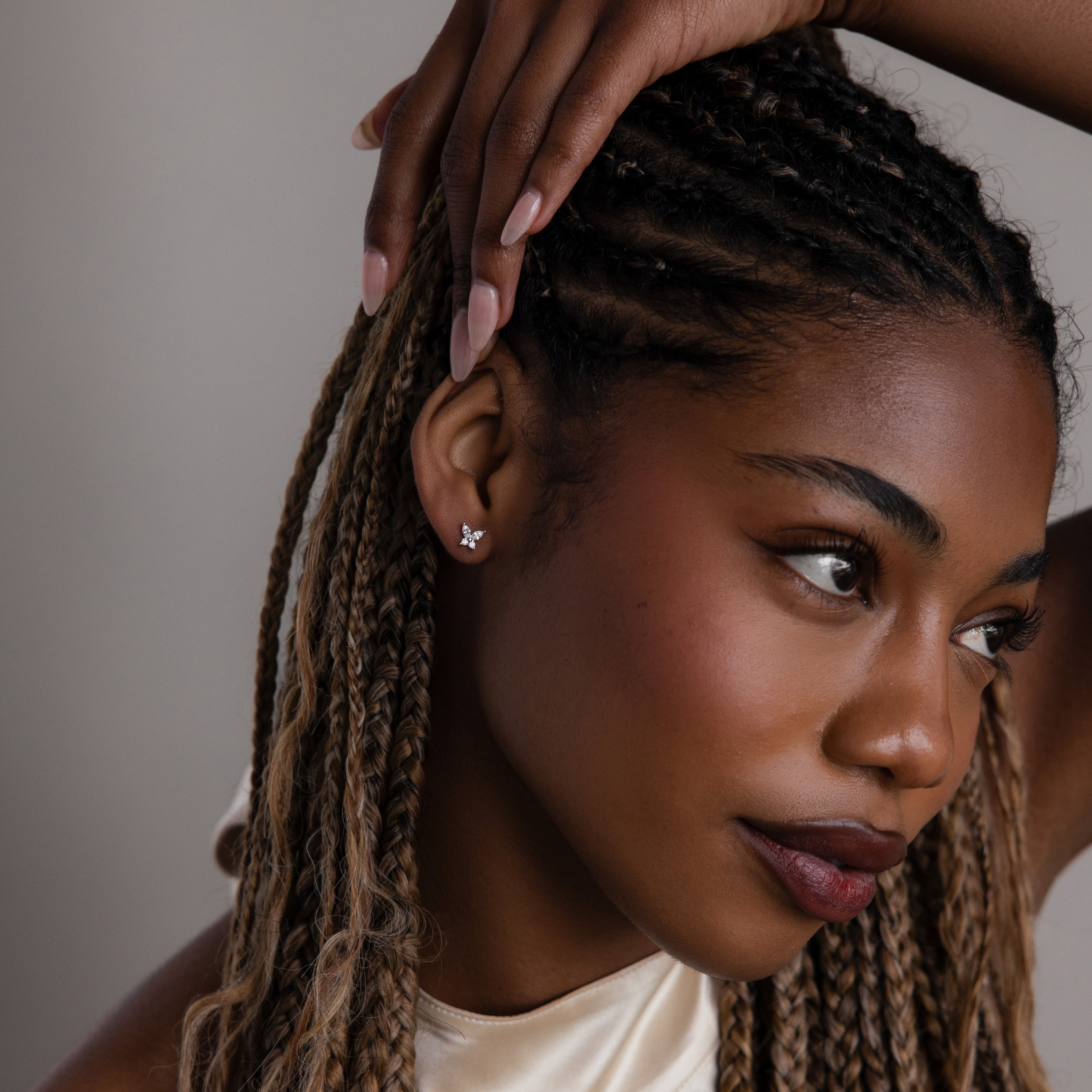 Woman with braided hair wearing a small diamond butterfly earring, looking to the side.