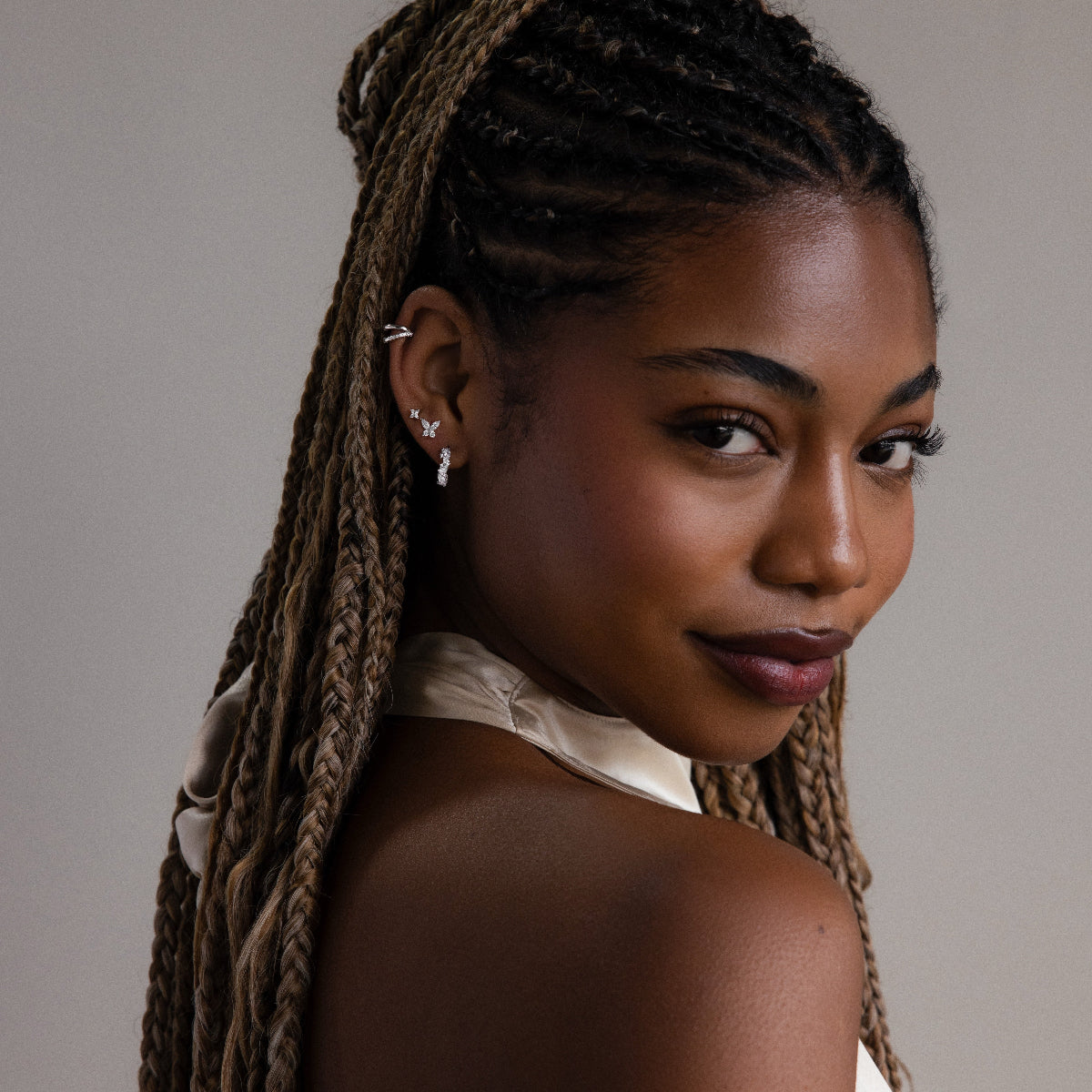 Woman with braided hair wearing various silver earrings against a neutral background