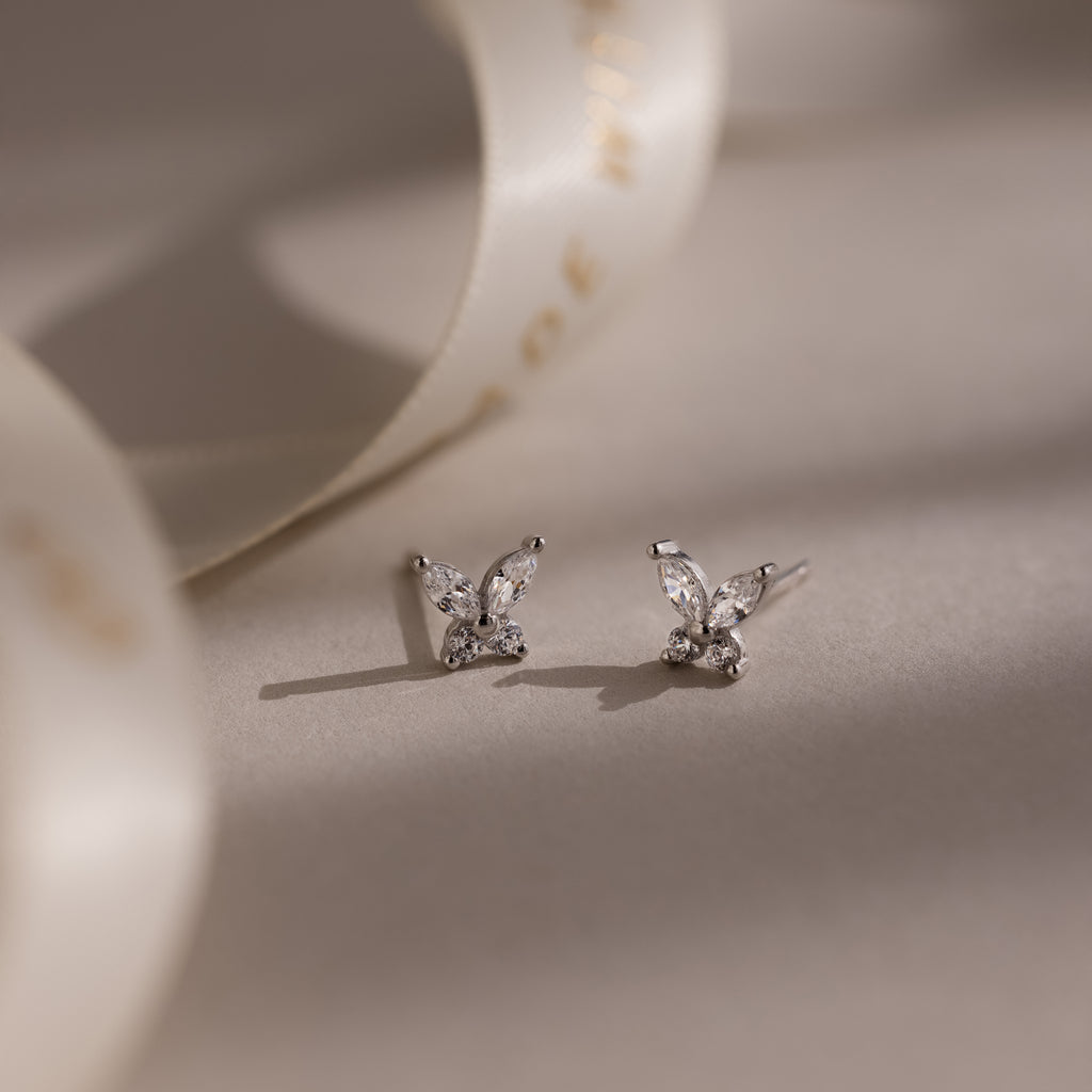Pair of diamond silver butterfly earrings on a soft beige background