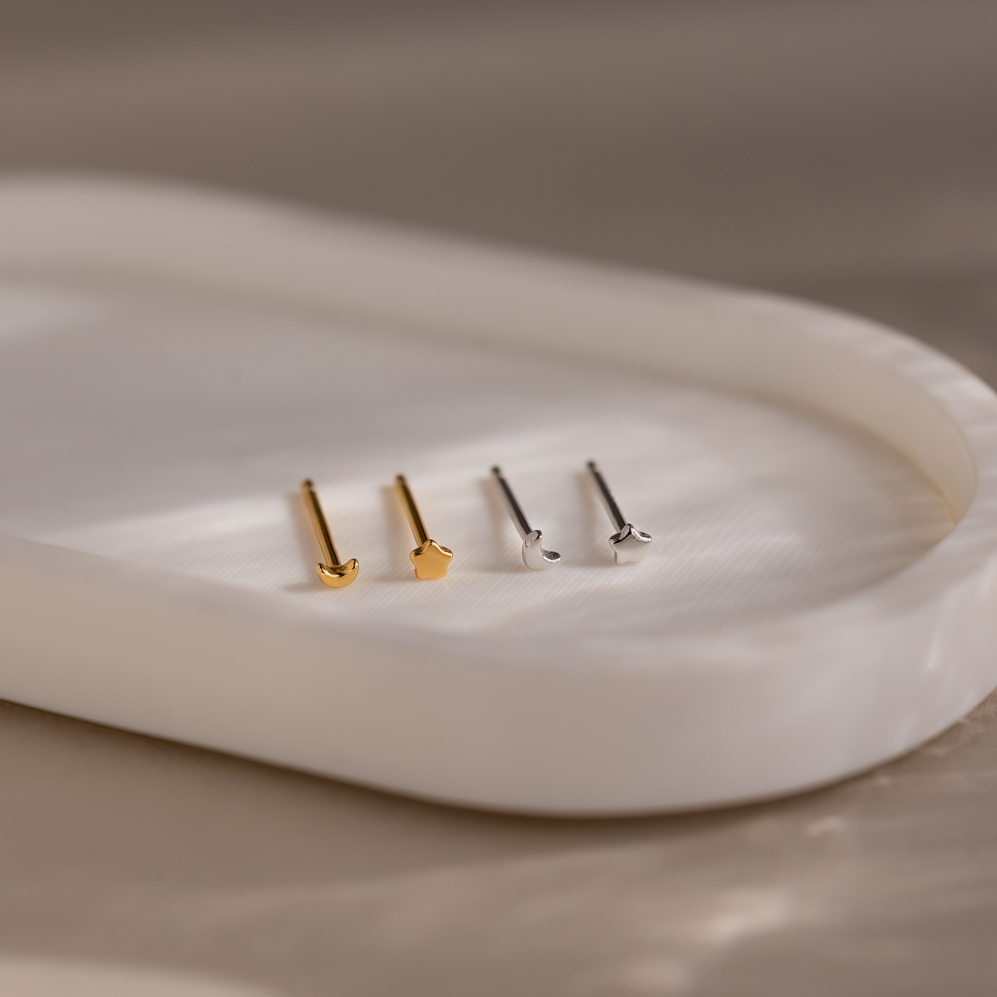 Two pairs of gold and silver moon and star earrings on a white plate with a neutral background