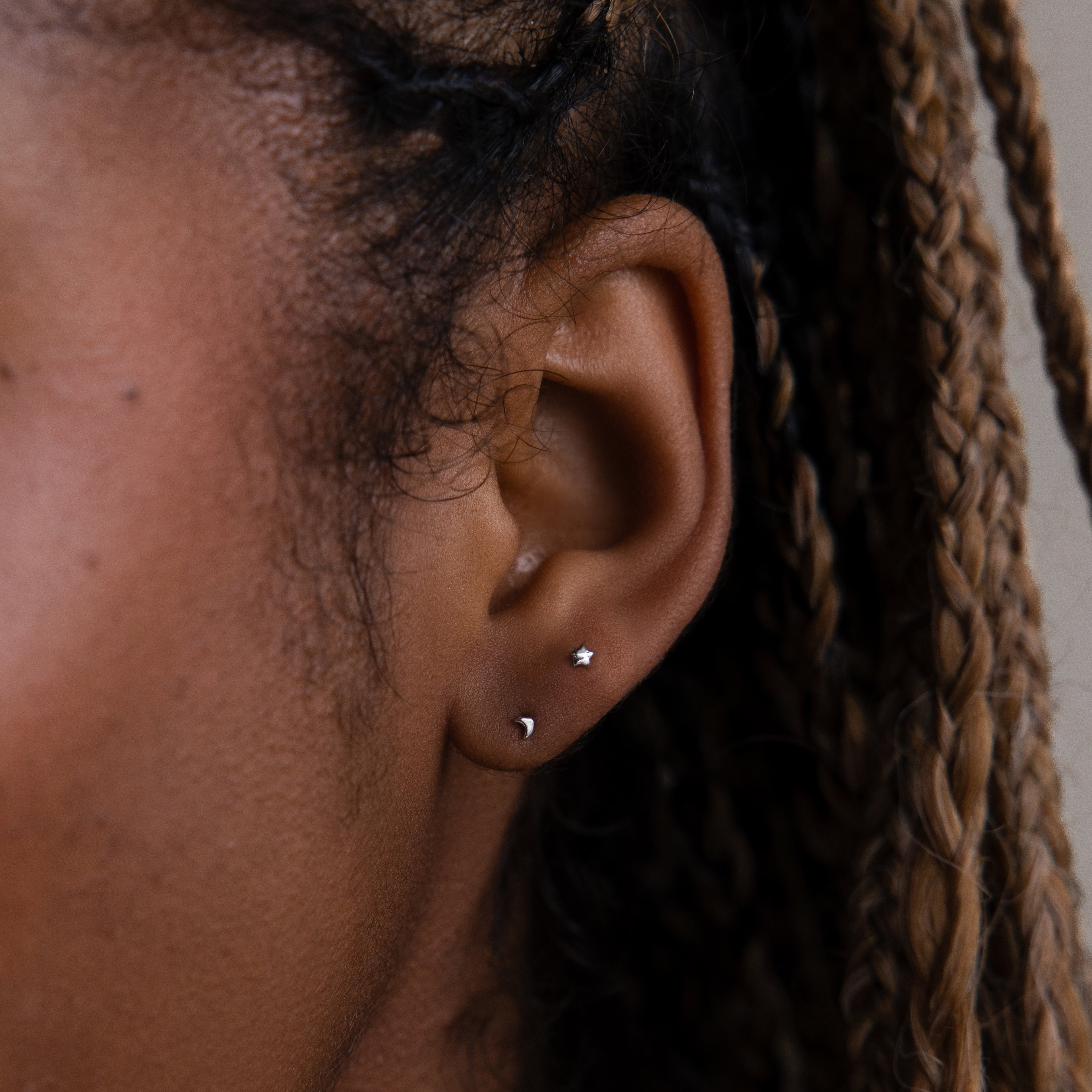 Close-up of an ear with two small moon and star earrings against a neutral background