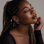 Woman with braided hair wearing various earrings against a neutral background