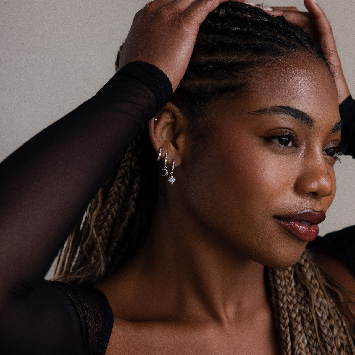 Woman with braided hair wearing various silver earrings against a neutral background