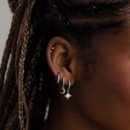 Close-up of an ear with silver hoop earrings and star-shaped earrings.