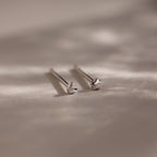Pair of tiny silver moon and star earrings on a beige fabric background