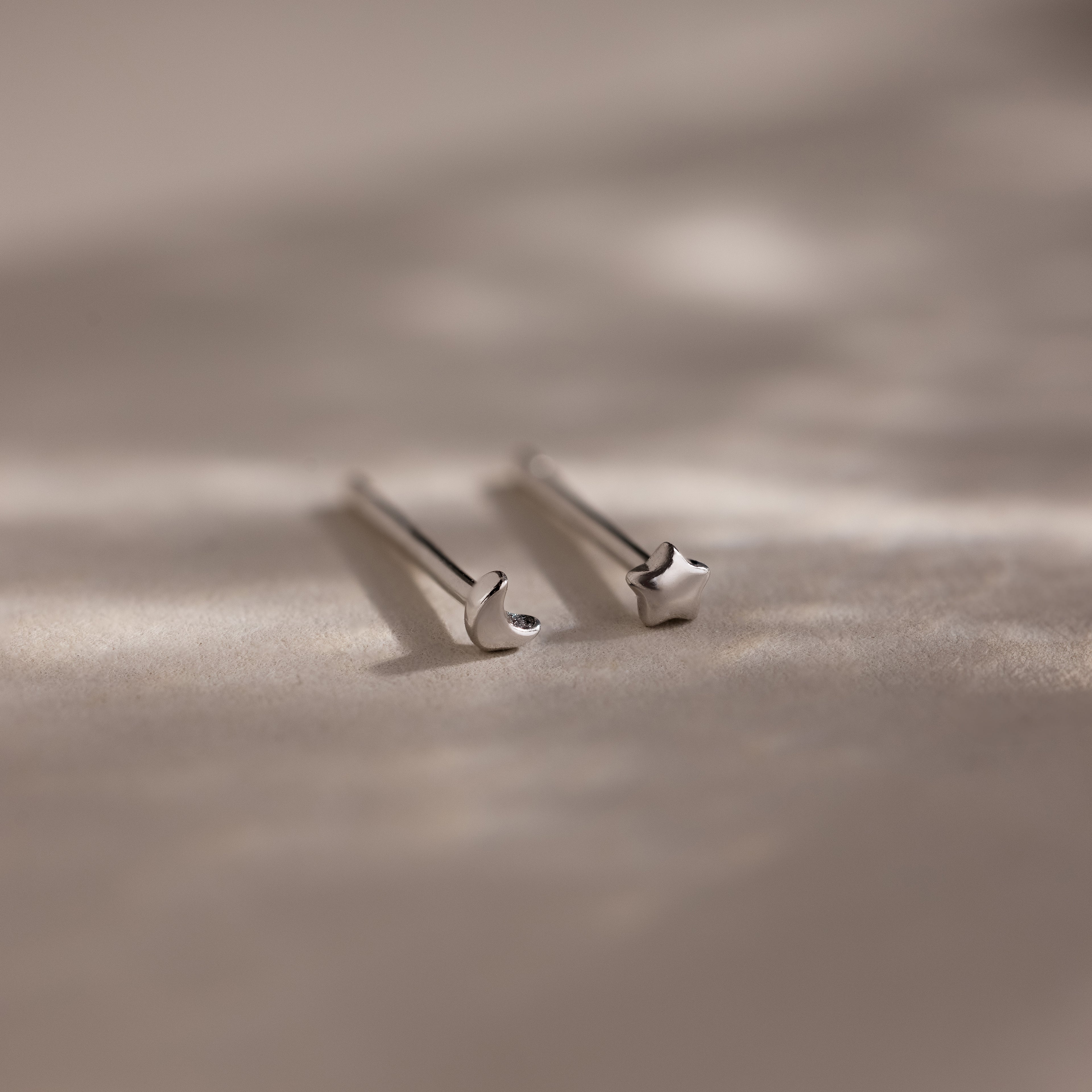 Pair of tiny silver moon and star earrings on a beige fabric background