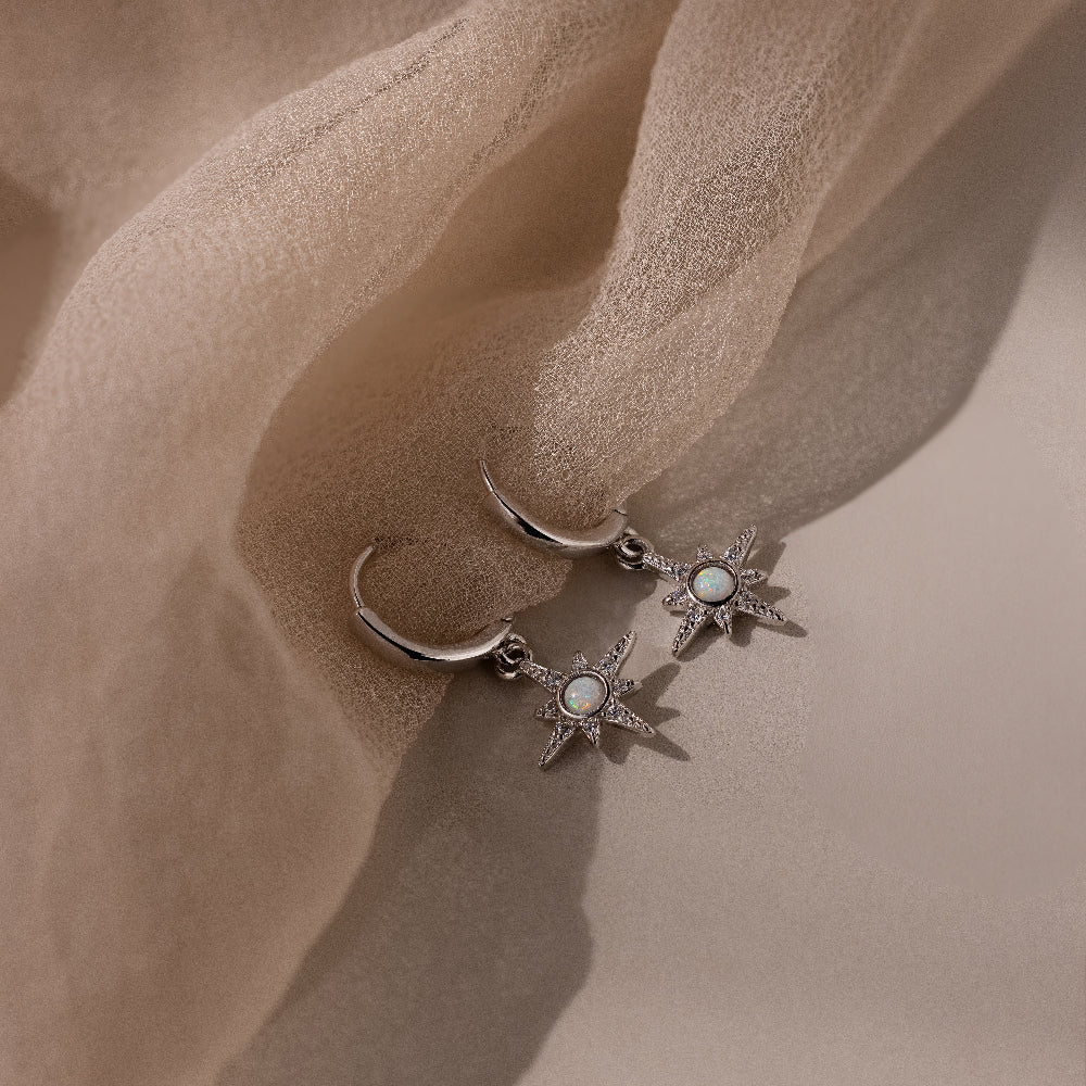 Pair of silver opal earrings with star designs on a beige fabric background