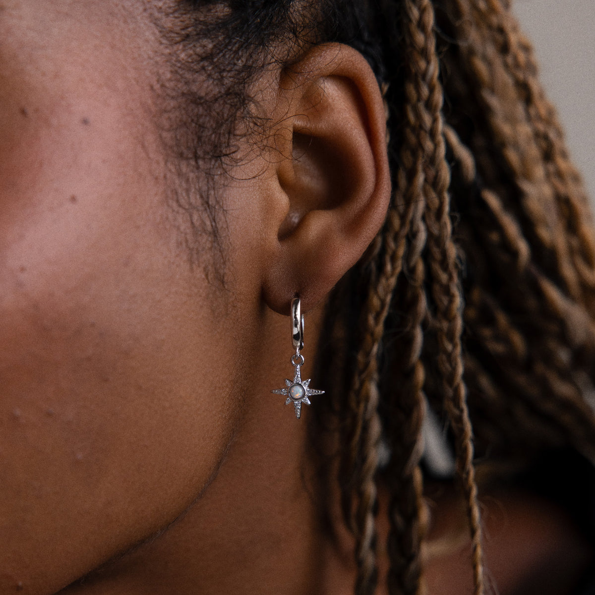 Close-up of a model wearing a silver star-shaped opal huggie hoop earring with braided hair.