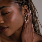 Close-up of a woman with braided hair wearing various silver diamond and opal earrings in a neutral background