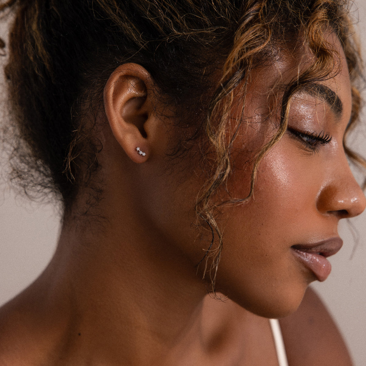 Close-up of a woman's face with silver diamond stud earrings in a neutral background