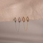 Two gold and silver hoop earrings with chain details on a beige background