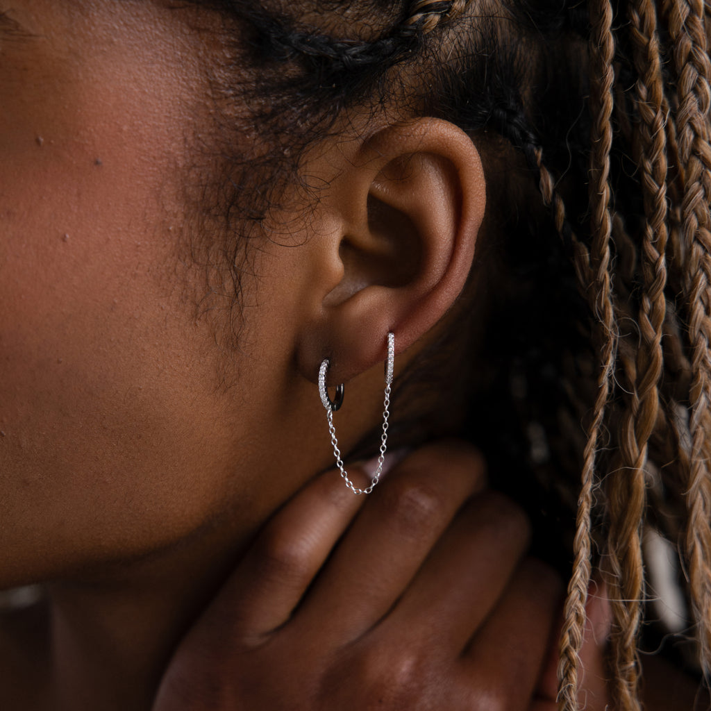 Close-up of a model with a silver double hoop chain earring, hand touching the face, and braided hair.