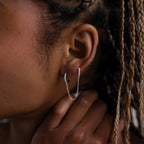 Close-up of a model with a silver double hoop chain earring, hand touching the face, and braided hair.