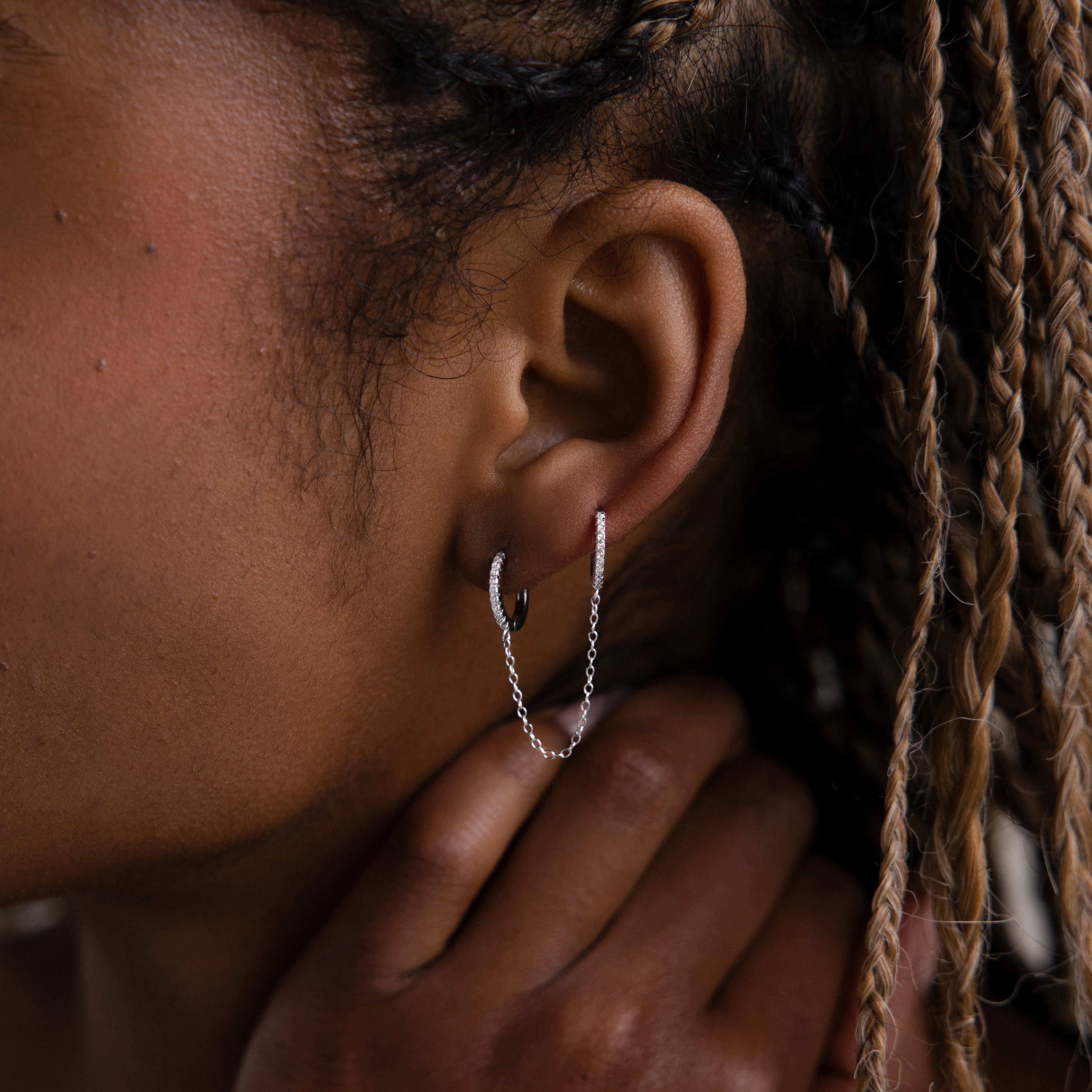 Close-up of a model with a silver double hoop chain earring, hand touching the face, and braided hair.