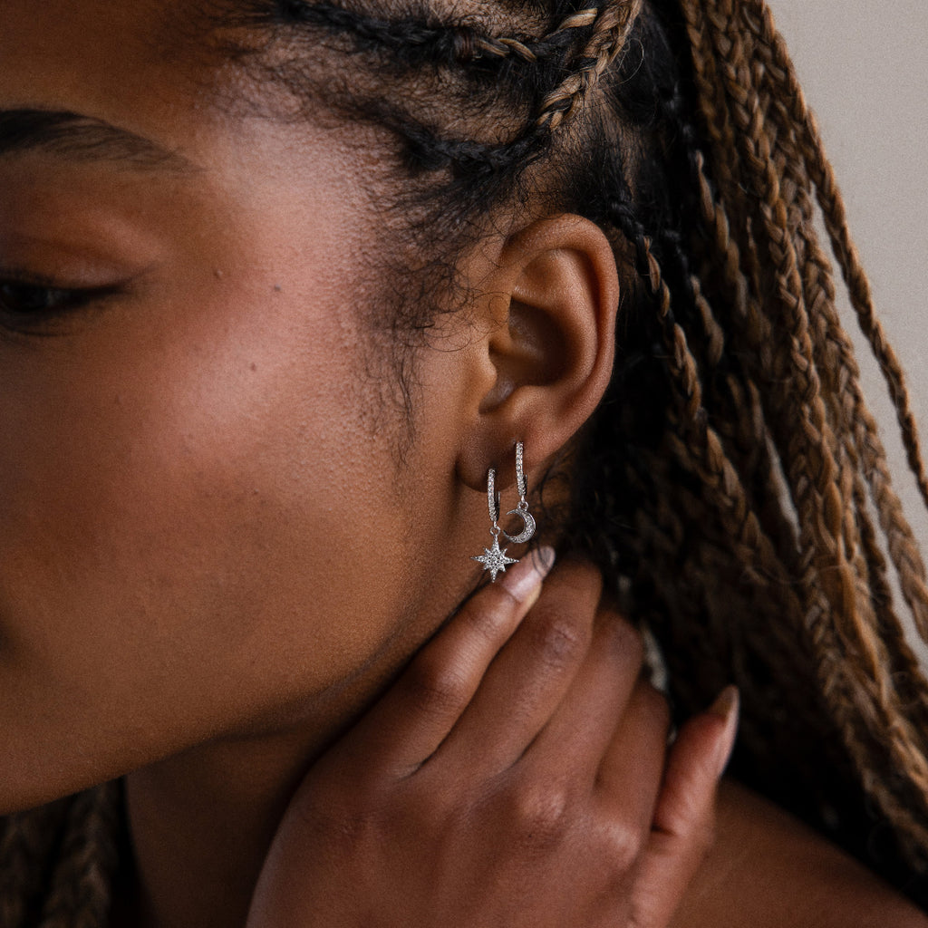 Close-up of a woman wearing silver moon and star hoop earrings with braided hair.