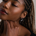 Close-up of a woman with braided hair wearing silver moon and star earrings, with a neutral background