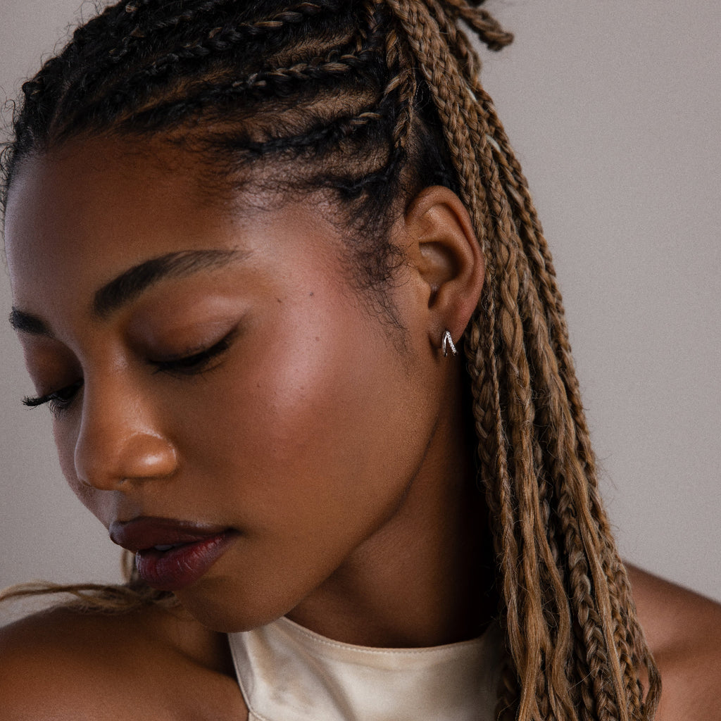 Woman with braided hair wearing a silver duo hoop earring against a neutral background
