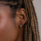 Close-up of an model with braided hair and a silver diamond huggie earring against a neutral background