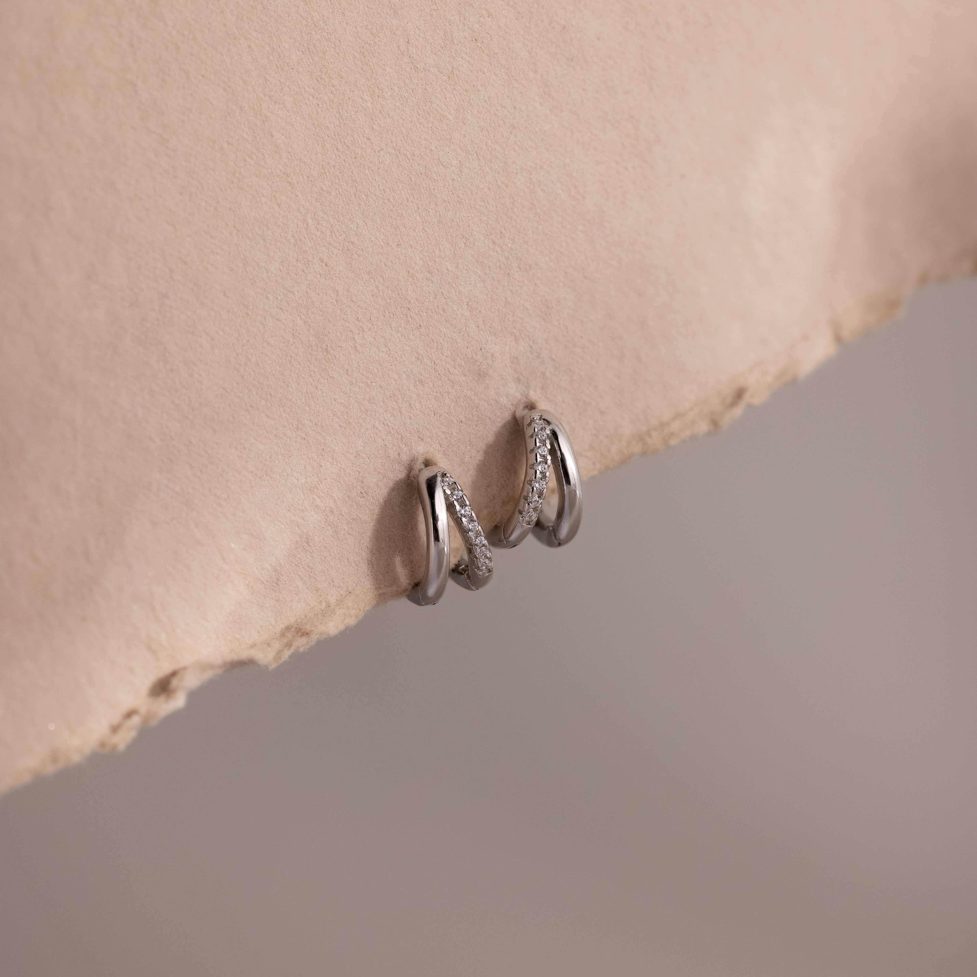 Pair of silver pave hoop earrings on a beige stone surface