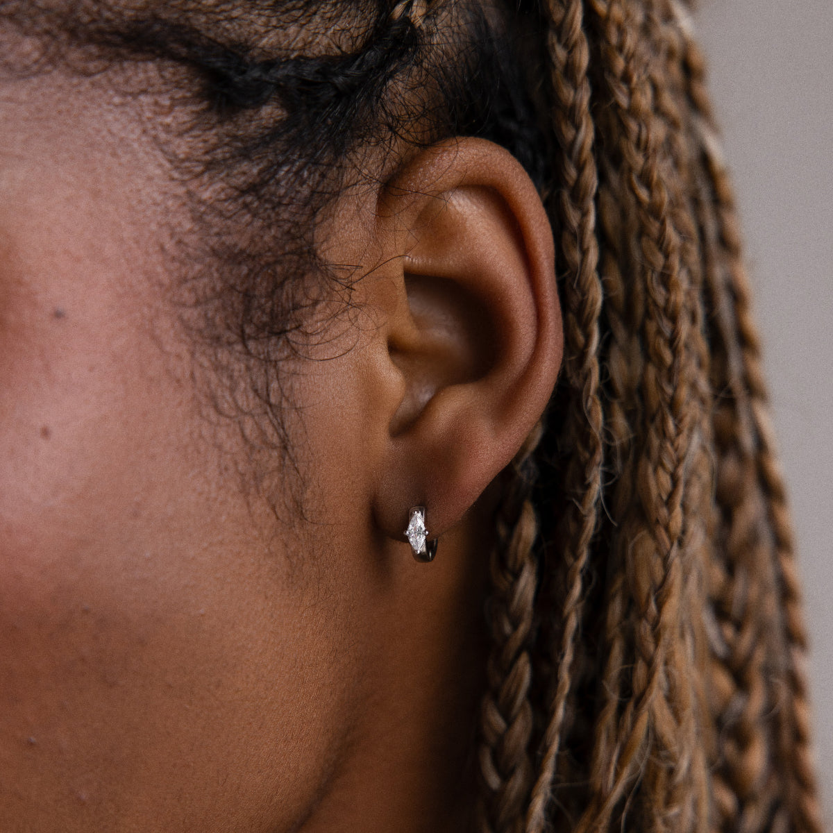 Close-up of an model with braided hair wearing a small silver marquise diamond hoop earring against a neutral background