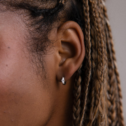 Close-up of an model with braided hair wearing a small silver marquise diamond hoop earring against a neutral background