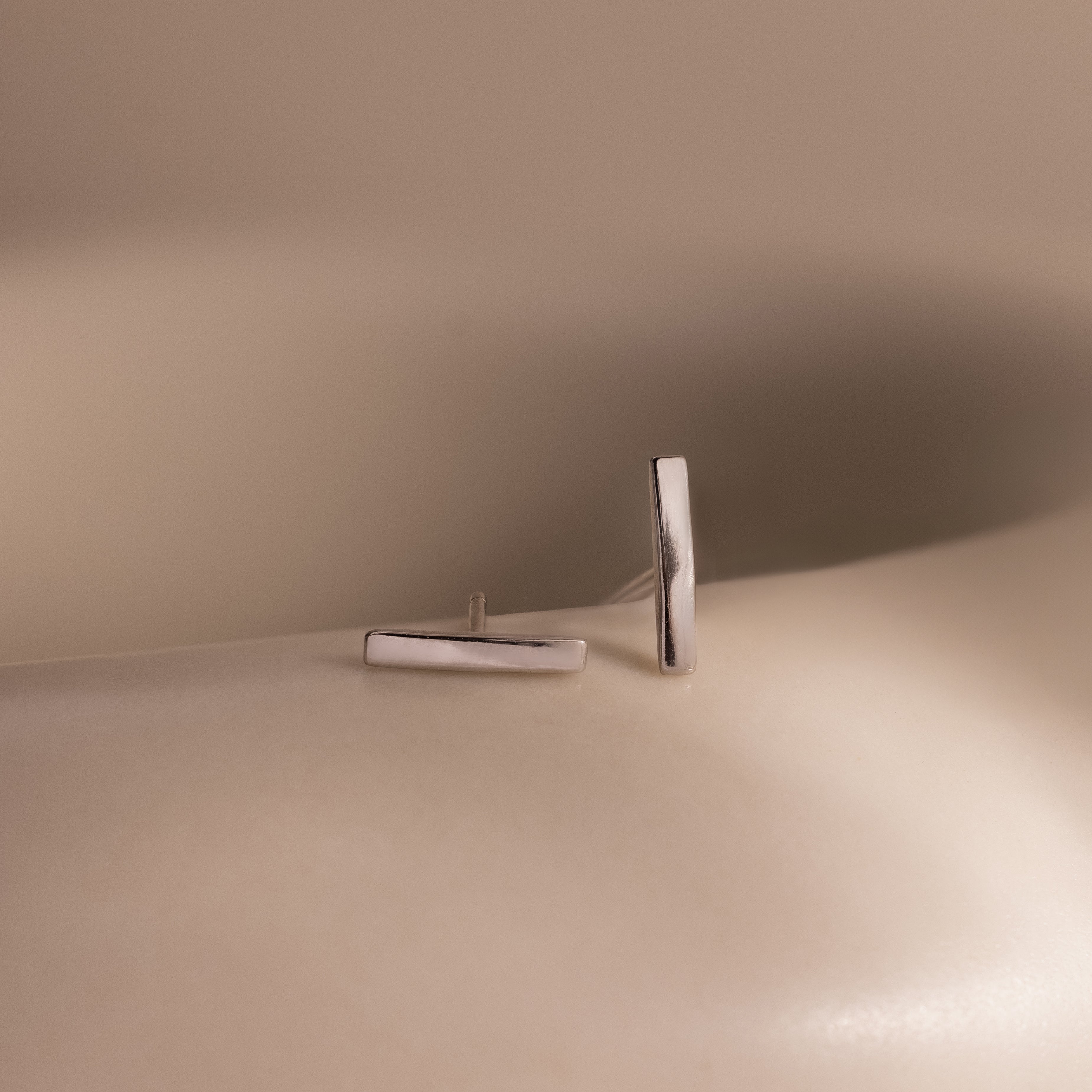 Pair of silver bar stud earrings on a beige surface with a neutral background
