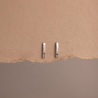Two silver bar earrings on a beige background