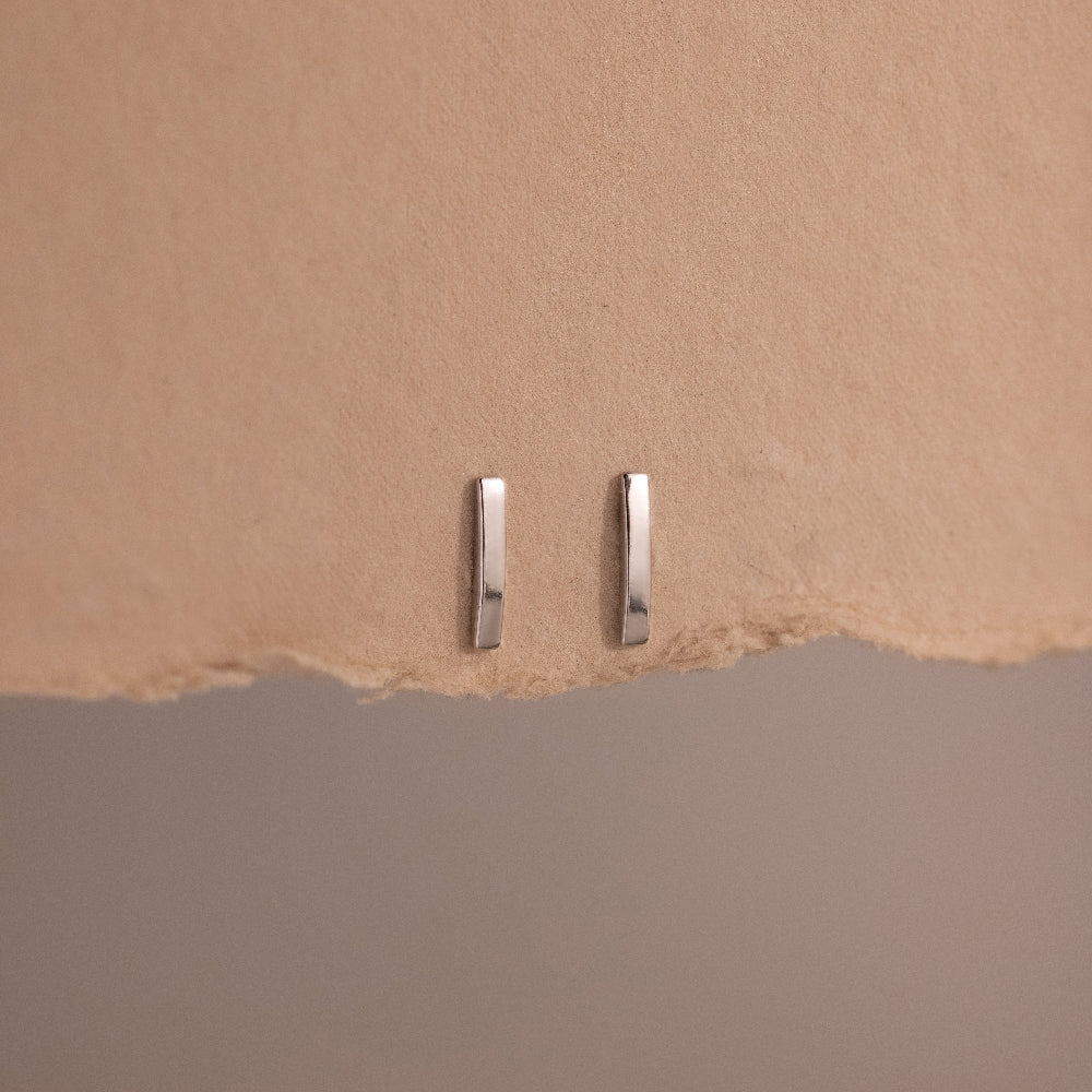 Two silver bar earrings on a beige background