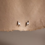 Pair of silver lightning bolt stud earrings on a beige fabric background