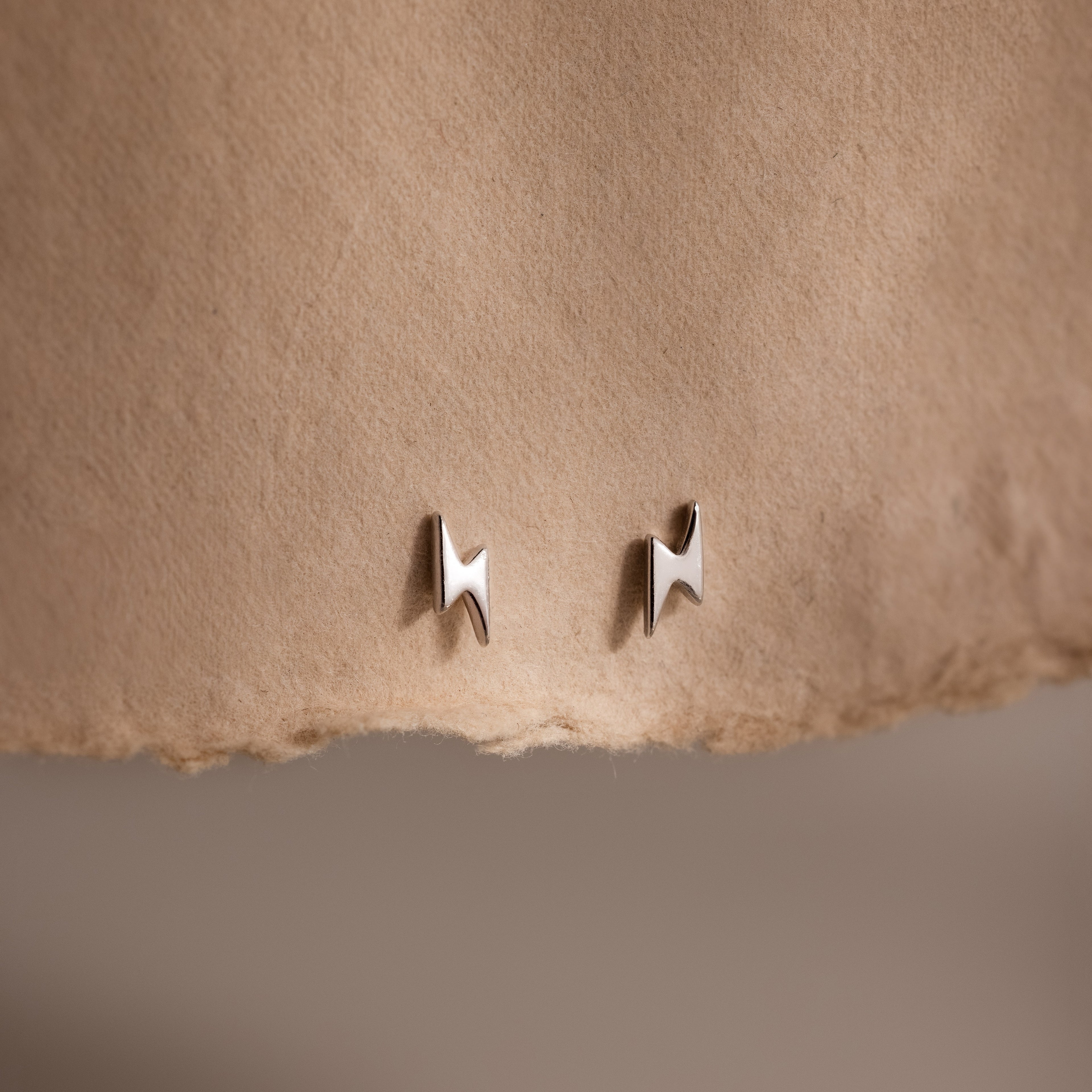 Pair of silver lightning bolt stud earrings on a beige fabric background
