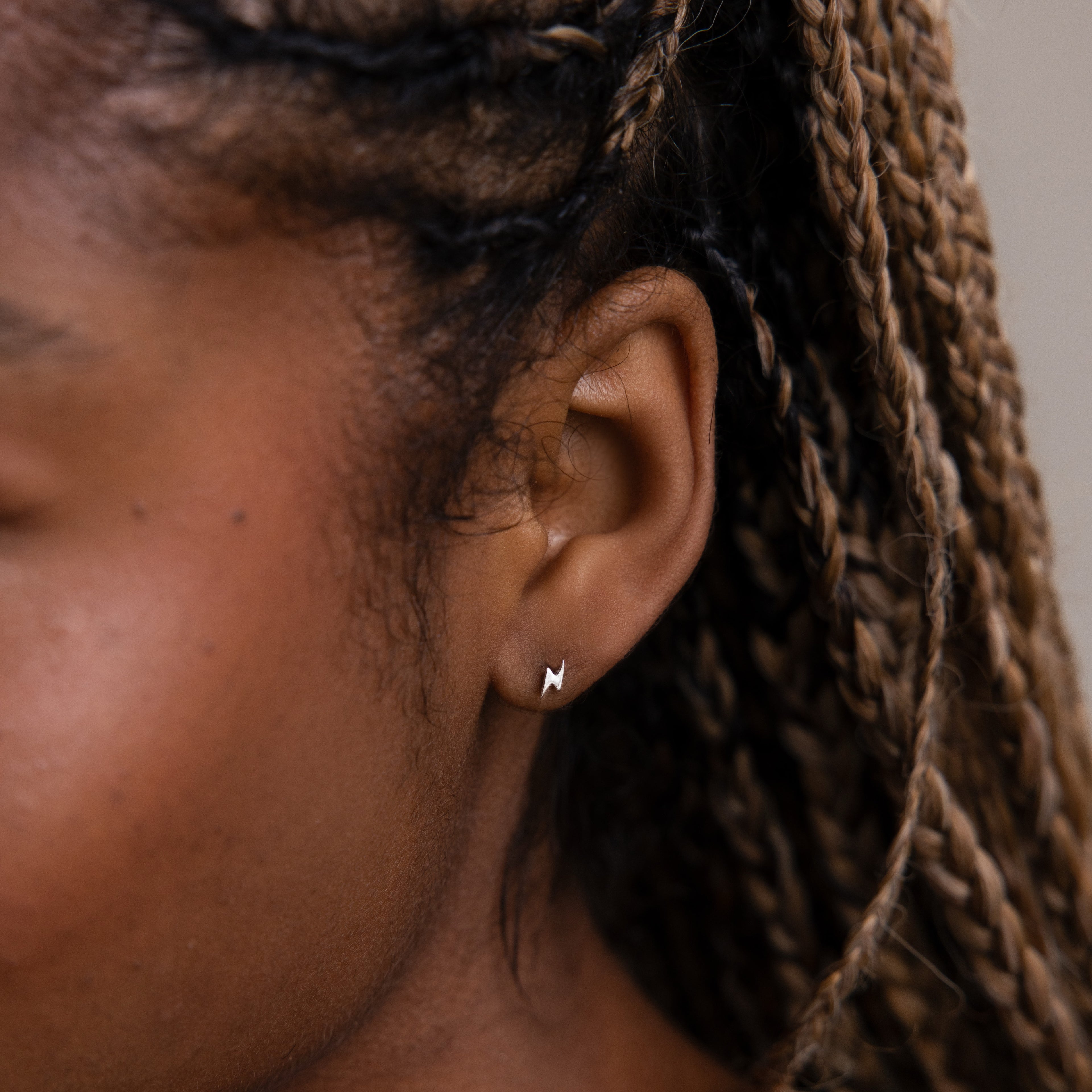 Model wearing small lightning bolt stud earrings in silver, styled as minimalist everyday jewelry on the ear.