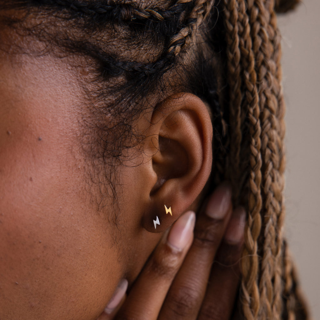 Close-up of a model with gold and silver lightning bolt stud earrings and braided hair.