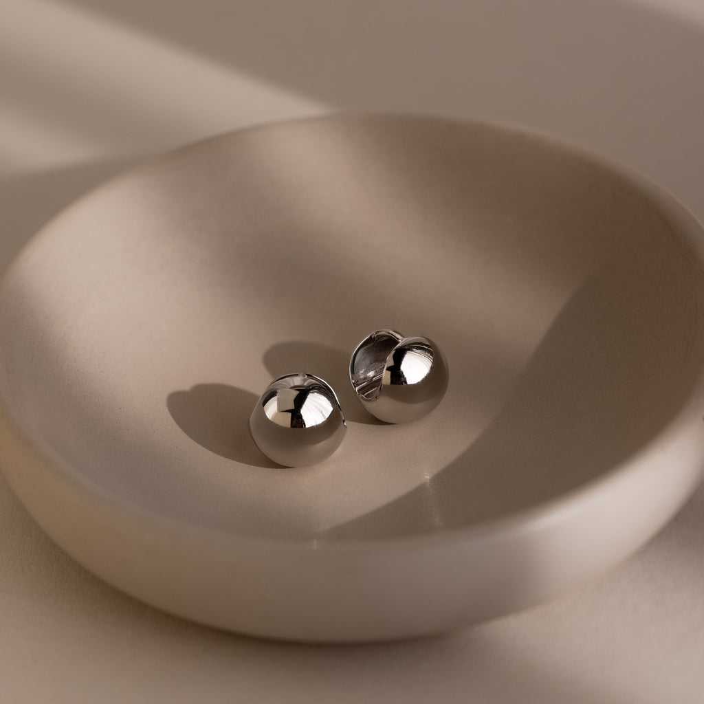 Two round silver earrings on a beige dish with a neutral background