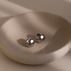 Two round silver earrings on a beige dish with a neutral background