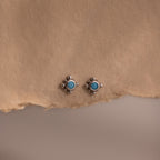 Pair of silver stud earrings with turquoise stones on a beige paper background