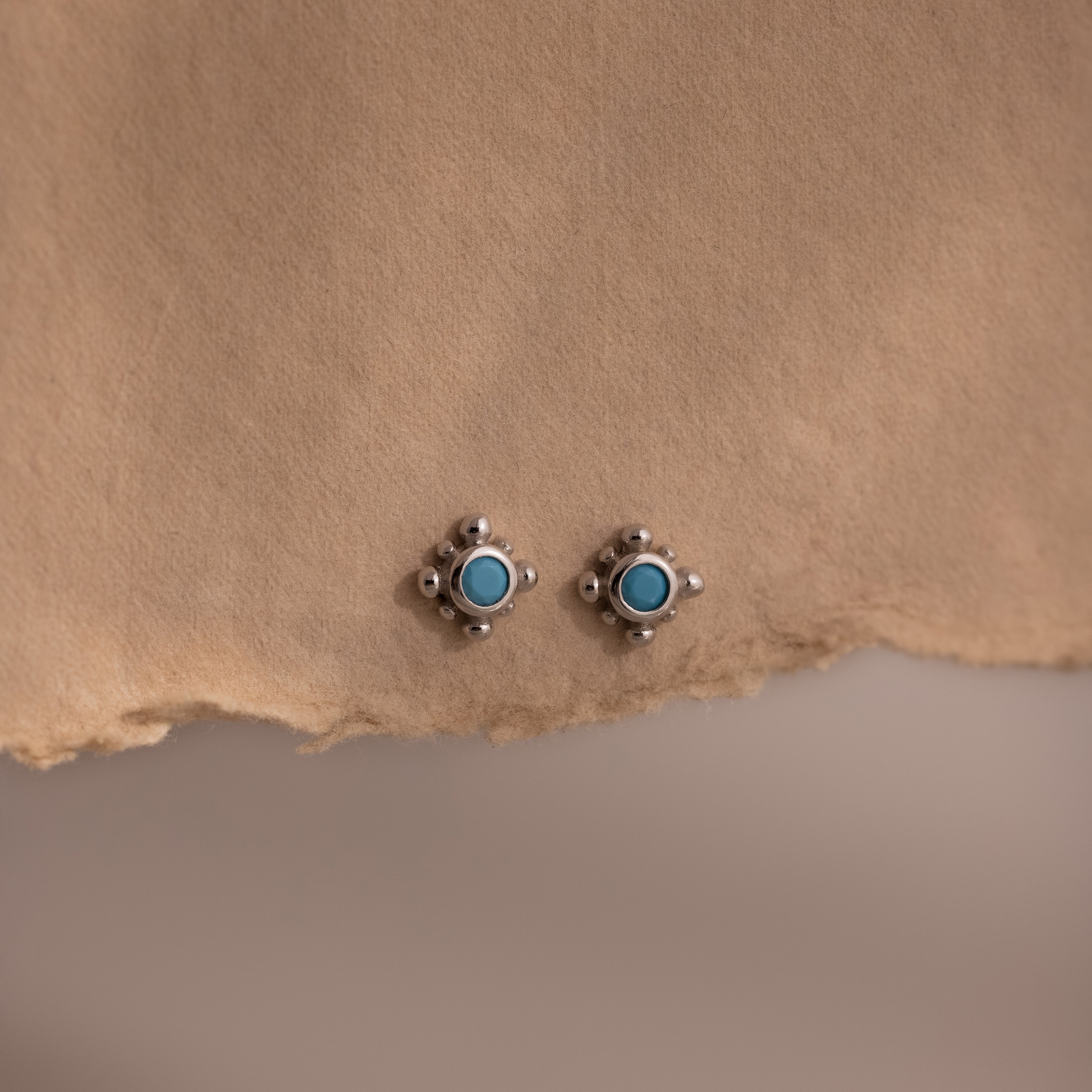Pair of silver stud earrings with turquoise stones on a beige paper background