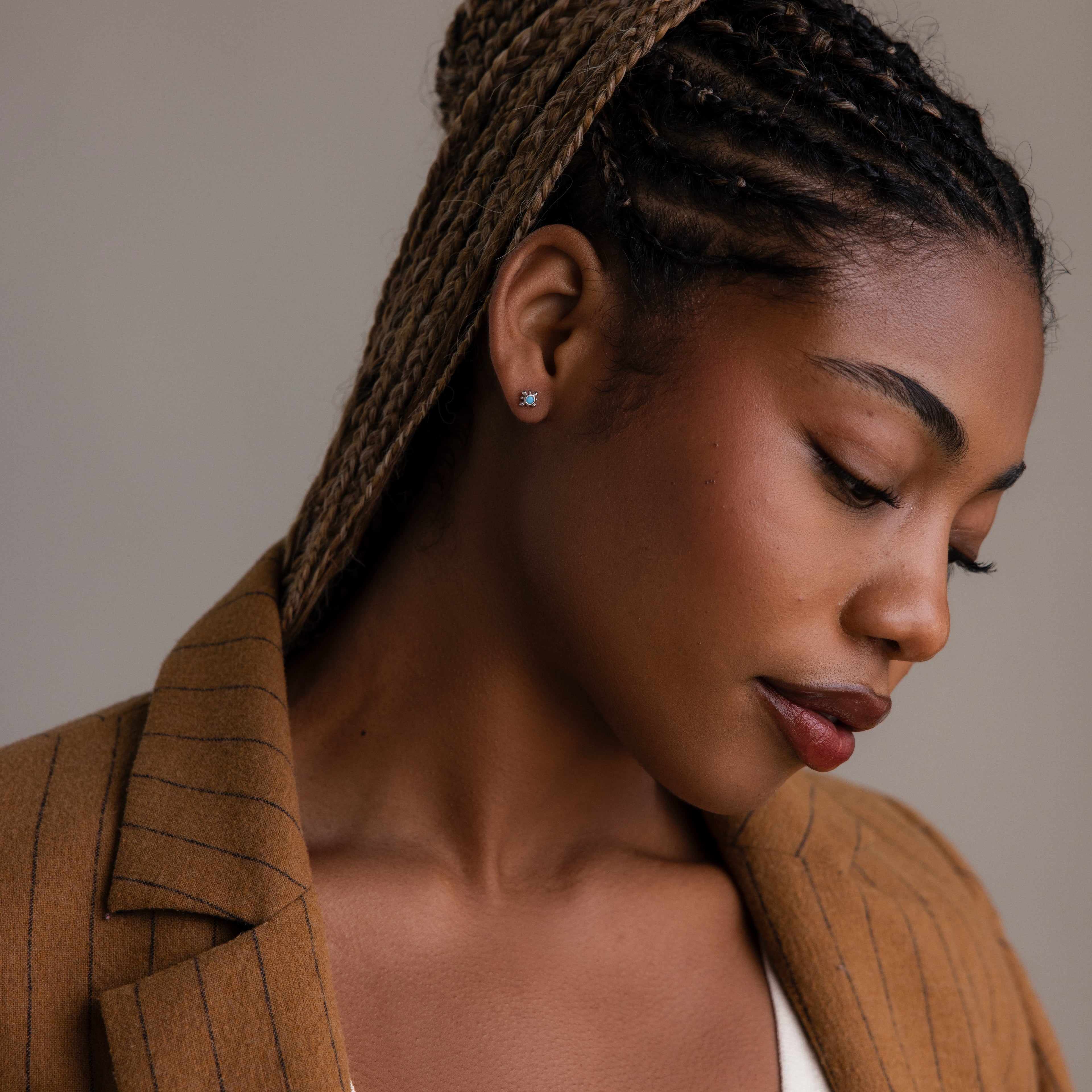 Woman wearing a brown pinstripe blazer and a silver turquoise stud earring with a neutral background