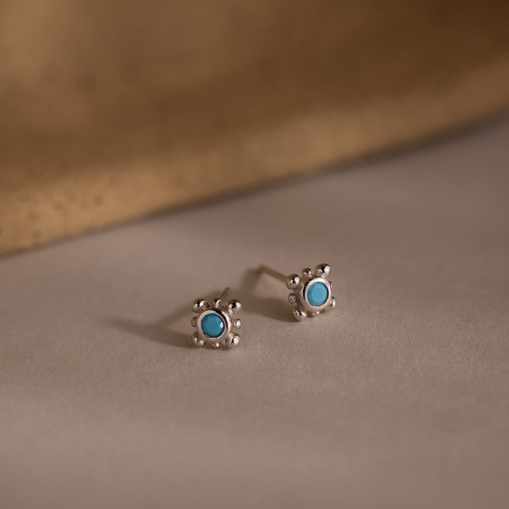 Pair of silver stud earrings with turquoise stones on a beige background