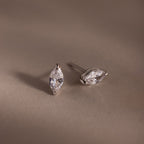 Pair of silver marquise-shaped diamond earrings on a beige background