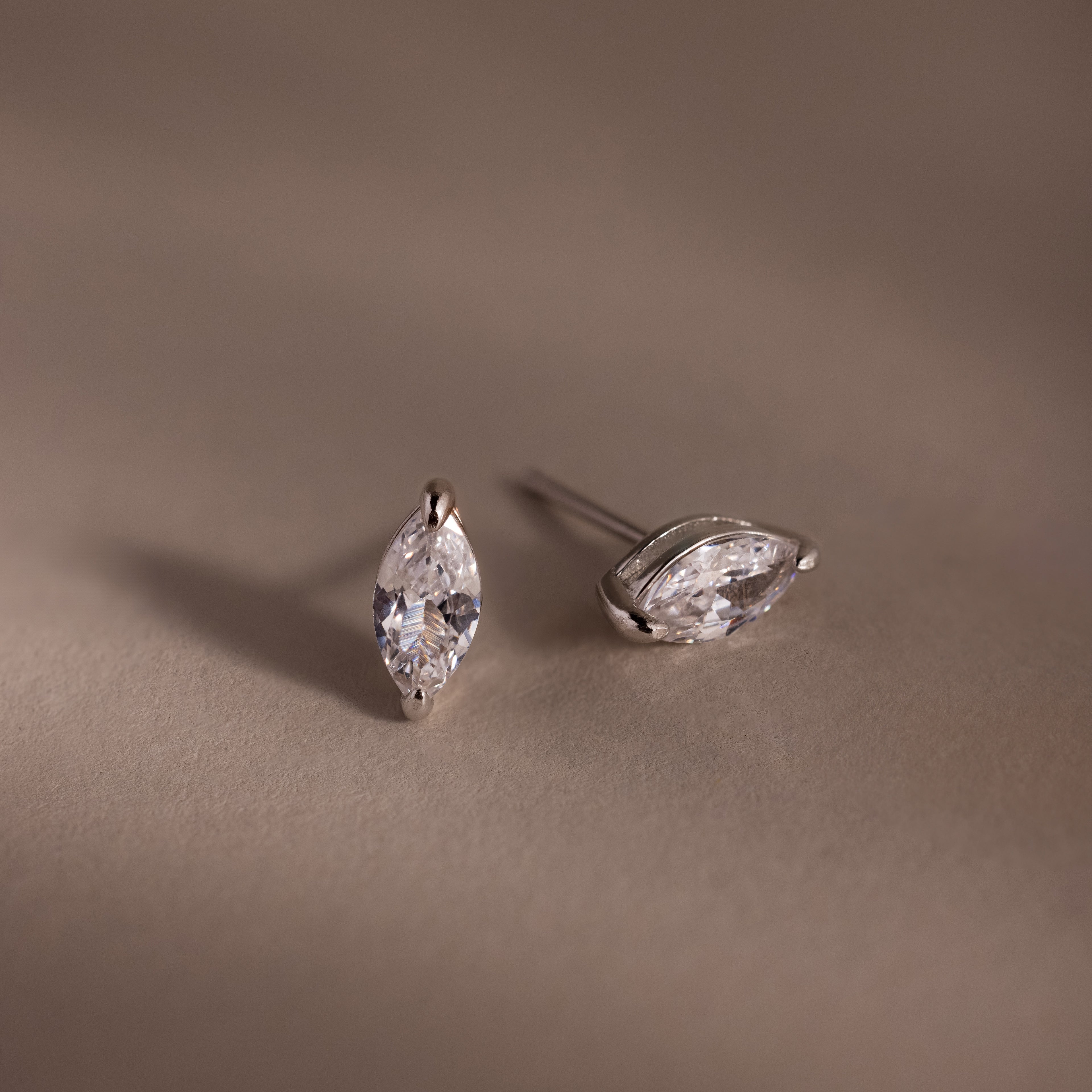 Pair of silver marquise-shaped diamond earrings on a beige background